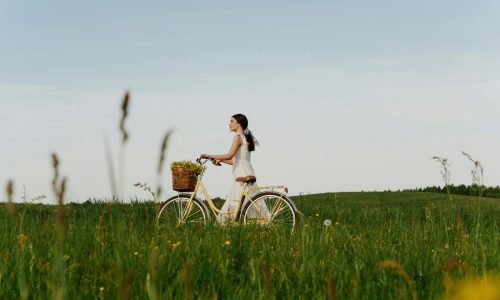 A teenage girl riding a bicycle through a lush green meadow on a sunny summer day.